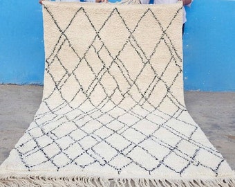 May include: A white and black Moroccan rug with a diamond pattern. The rug has a fringe border.