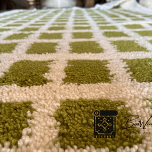May include: Close-up of a green and white checkered rug with a fluffy texture. The rug is made of wool and has a modern design.