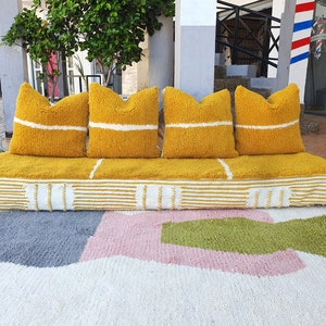 May include: A yellow and white striped couch with four yellow pillows with white stripes. The couch is sitting on a white rug with pink and green geometric shapes.