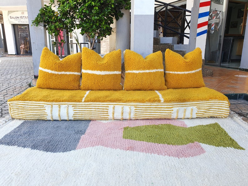 May include: A yellow and white striped couch with four yellow pillows with white stripes. The couch is sitting on a white rug with pink and green geometric shapes.