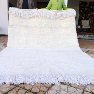 K&ouml;nnte beinhalten: Ein wei&szlig;er, flauschiger Teppich mit Fransenrand. Der Teppich wird von zwei Personen gehalten.