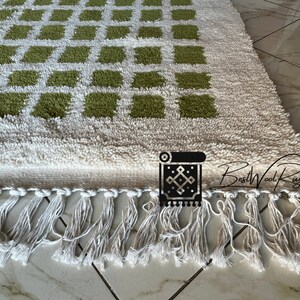 May include: A white and green wool rug with a geometric pattern. The rug has a fringe border and the text "BestWoolRug" is visible in the bottom right corner.