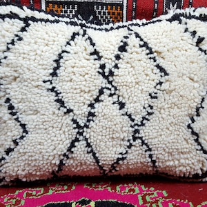 May include: White and black Moroccan pouf cushion with a diamond pattern. The cushion is made of a fluffy, textured fabric.