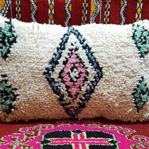 May include: White throw pillow with a diamond pattern in black, blue, pink, and green. The pillow is made of a fluffy, textured fabric.
