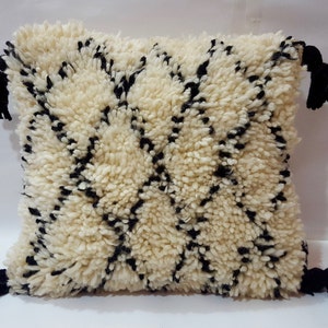 May include: A white and black patterned throw pillow with black tassels. The pillow is made of a fluffy, textured fabric.