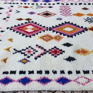 May include: A white rug with a colorful geometric pattern. The pattern features diamonds, triangles, and other shapes in shades of pink, red, blue, yellow, and black.