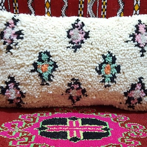 May include: A white throw pillow with a tufted texture and embroidered floral designs in pink, green, and orange.