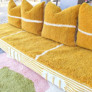 May include: A yellow tufted sofa with white stripes along the edges and four yellow tufted pillows with white stripes. The sofa is on a multi-colored rug.