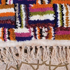 May include: A colorful, hand-woven rug with a geometric pattern and fringe. The rug is made of wool and has a variety of colors, including red, orange, yellow, green, blue, and purple.