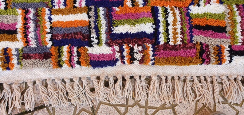 May include: A colorful, hand-woven rug with a geometric pattern and fringe. The rug is made of wool and has a variety of colors, including red, orange, yellow, green, blue, and purple.