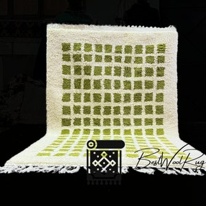May include: A white wool rug with a geometric pattern of green squares. The rug has a fringe border and the text "BestWoolRug" is visible in the bottom right corner.