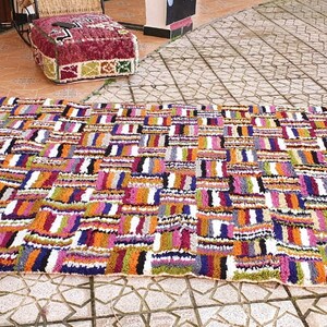 May include: A colorful Moroccan rug with a geometric pattern in shades of orange, pink, purple, green, and white. The rug has a white background and is made of wool.