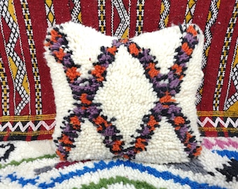 May include: White throw pillow with a geometric pattern in orange, purple, and black. The pillow is made of a fluffy, textured fabric.