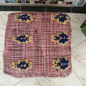 May include: A red, woven floor cushion with a tufted design. The cushion has five yellow and blue floral patterns.