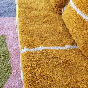 May include: A close-up of a yellow and white striped rug with a white stripe running across the center. The rug is made of a soft, fluffy material.