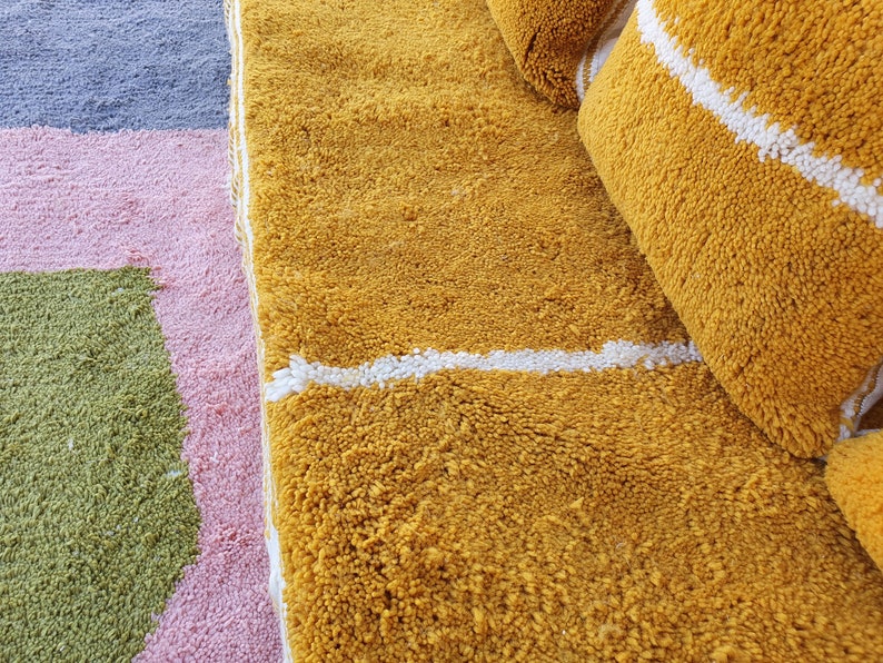 May include: A close-up of a yellow and white striped rug with a white stripe running across the center. The rug is made of a soft, fluffy material.