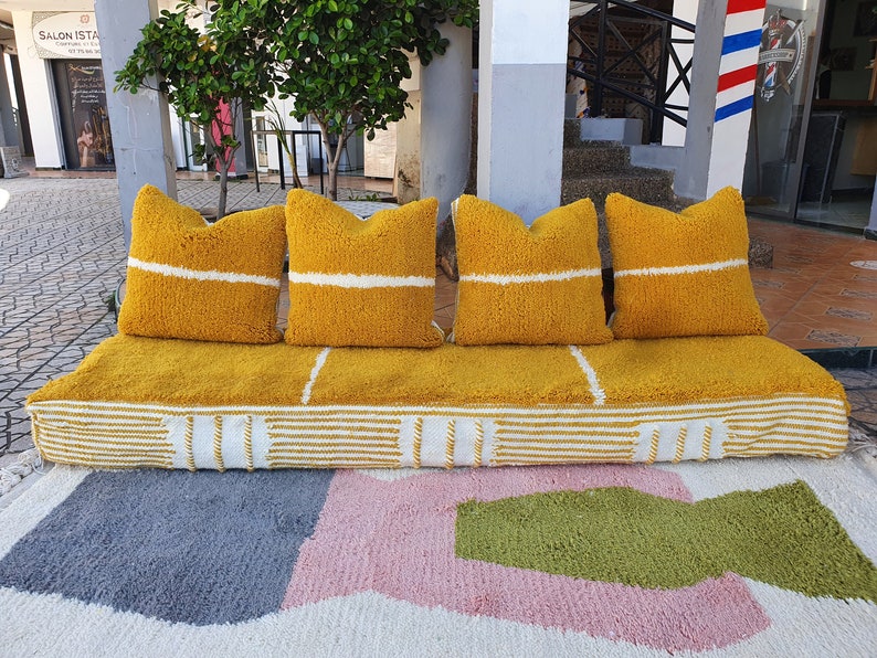 May include: A yellow tufted sofa with white stripes and four matching pillows. The sofa is sitting on a white rug with pink, gray, and green geometric shapes.