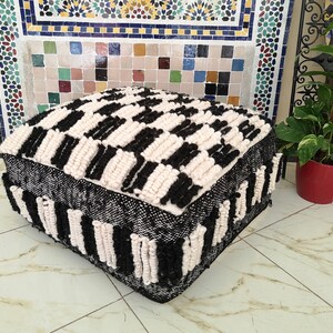 May include: Black and white woven pouf with a checkered pattern. The pouf is made of thick, fluffy yarn and has a square shape.