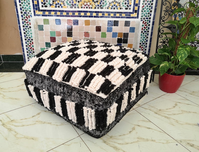 May include: Black and white woven pouf with a checkered pattern. The pouf is made of thick, fluffy yarn and has a square shape.