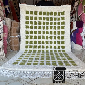 May include: A white and green Moroccan rug with a geometric pattern of squares. The rug has a fringe border and is made of wool.