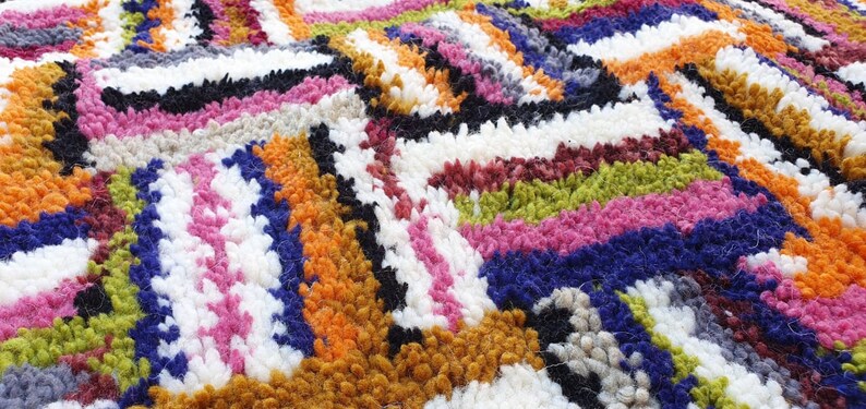 May include: A colorful, geometric rug with a variety of textures and patterns. The rug is made of different colored yarns woven together to create a unique and eye-catching design.