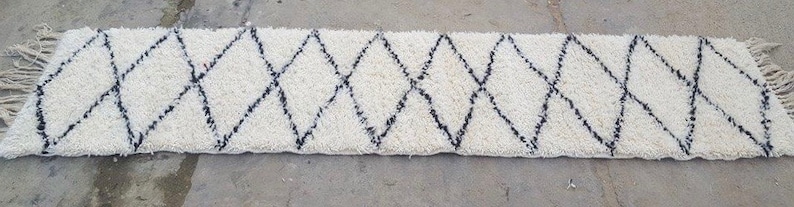 K&ouml;nnte beinhalten: Ein wei&szlig;er und schwarzer Teppich mit Rautenmuster und Fransen an den Enden. Der Teppich ist aus einem weichen, flauschigen Material.