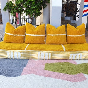 May include: A yellow and white striped couch with four yellow pillows. The couch is sitting on a white rug with pink and green geometric shapes.