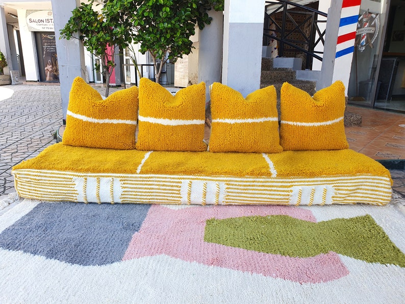 May include: A yellow and white striped couch with four yellow pillows. The couch is sitting on a white rug with pink and green geometric shapes.