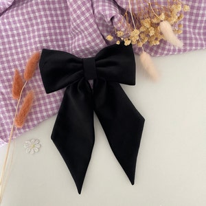 Puede incluir: Un lazo para el cabello de color negro s&oacute;lido que presenta una secci&oacute;n superior ancha y estructurada, junto con dos colas largas y puntiagudas que se extienden hacia abajo. El lazo est&aacute; hecho de una tela lisa y mate con dise&ntilde;o sim&eacute;trico.