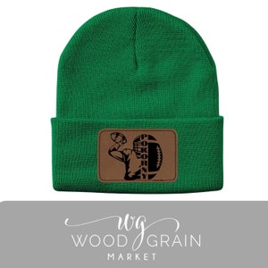 May include: Green knit beanie with a brown leather patch featuring a silhouette of a football player with the text "Pokorny" inside the football.