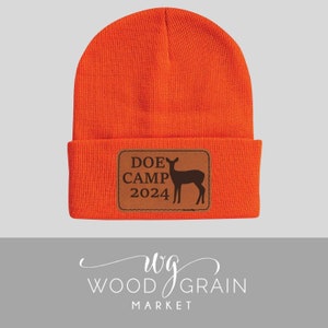 May include: Orange knit beanie with a brown leather patch that says "DOE CAMP 2024" and has a silhouette of a deer.