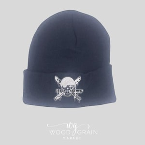 Puede incluir: Gorro de punto azul marino con un diseño de calavera y huesos cruzados en blanco. El gorro es de estilo con dobladillo, hecho de un material de punto suave. El diseño de la calavera tiene detalles de goteo.