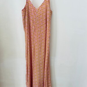 May include: A long pink and gold patterned maxi dress with thin straps and a V-neckline.