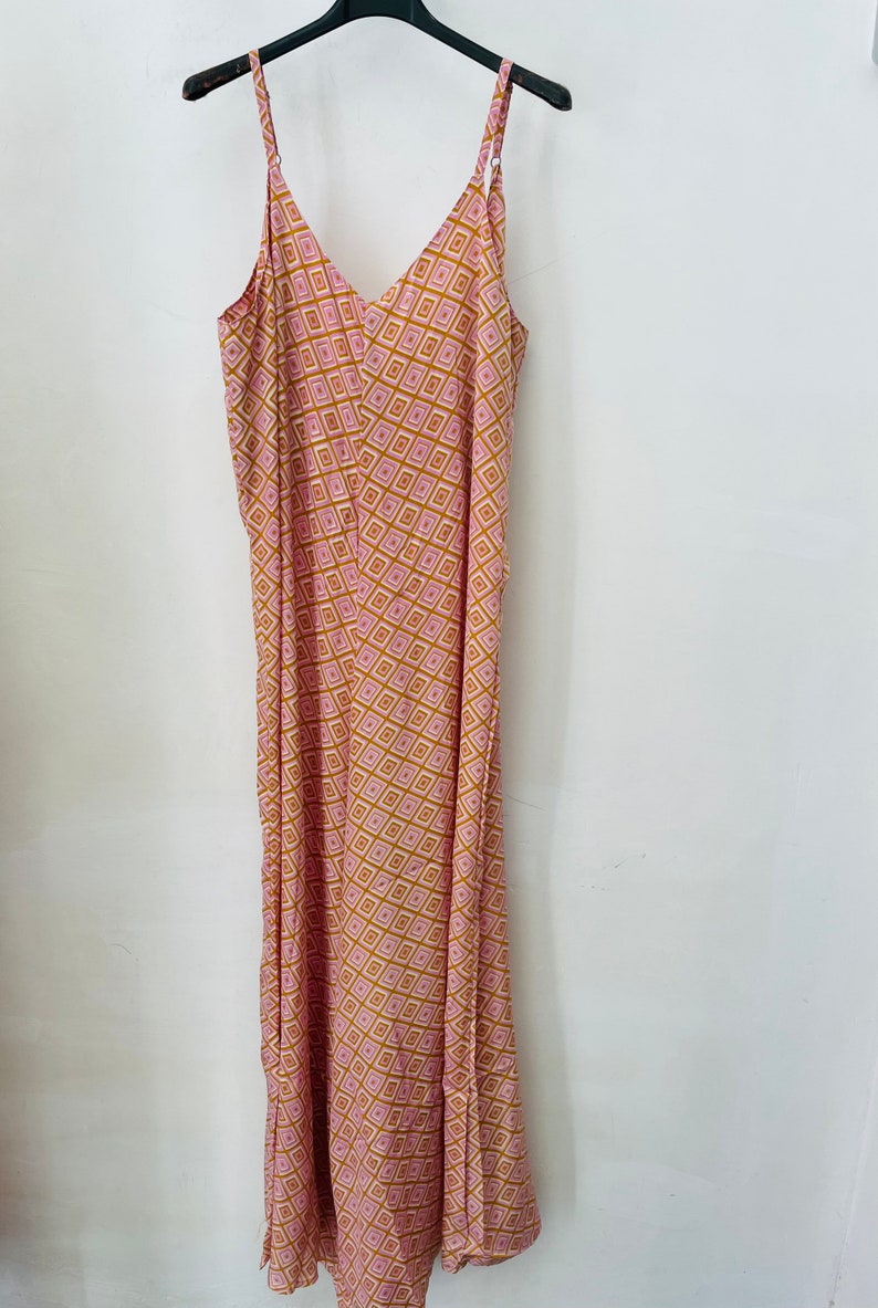 May include: A long pink and gold patterned maxi dress with thin straps and a V-neckline.