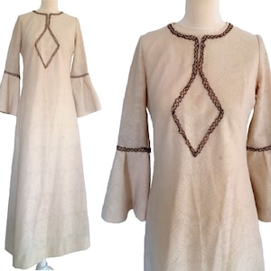 May include: A long, white maxi dress with a diamond-shaped design on the front. The dress has long sleeves with bell bottoms and brown trim around the neckline and sleeves.