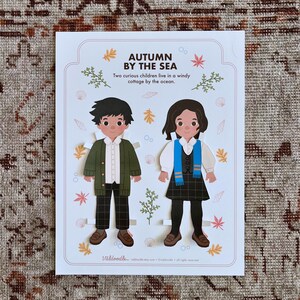 May include: A paper doll set featuring two children dressed in autumn clothing. The boy is wearing a green jacket, white shirt, and plaid pants. The girl is wearing a white shirt, blue scarf, and plaid skirt. The text on the paper doll set reads "Autumn by the Sea. Two curious children live in a windy cottage by the ocean."