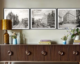 May include: Three black and white framed photographs of cityscapes. The photos are hung on a wall above a dark brown wooden cabinet with three drawers. The cabinet has a decorative grooved design.