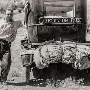 May include: A black and white photo of a man standing next to a vintage car with the words "Oregon or Bust" written on the back. The car is loaded with luggage and has a license plate that reads "SEDAN 1938 52-2409".