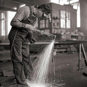 May include: A worker wearing a welding mask and protective clothing uses a torch to weld metal. Sparks fly from the welding process.