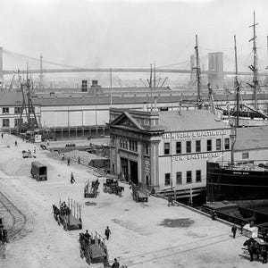 May include: A black and white photo of a busy New York City harbor scene.  A large ship is docked at a pier with a building that reads "New York & Baltimore Steamship Company For Baltimore".  The Brooklyn Bridge is visible in the background.