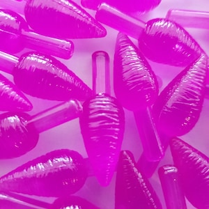 May include: A collection of bright pink, carrot-shaped Christmas light bulbs. Each bulb has a ridged body and a clear, cylindrical base. The bulbs are scattered across a white surface, creating a festive and colorful display.