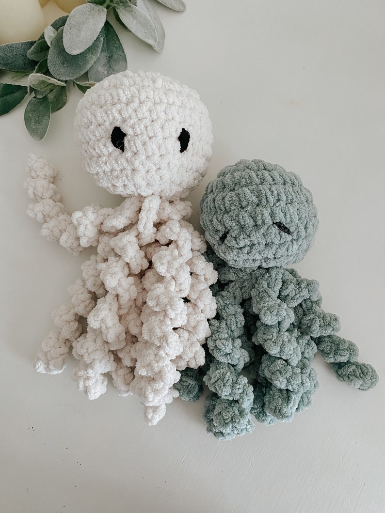 Puede incluir: Dos peluches de pulpo tejidos a crochet, uno en blanco y otro en verde azulado. Ambos tienen ojos negros y est&aacute;n hechos con un hilo suave y esponjoso.