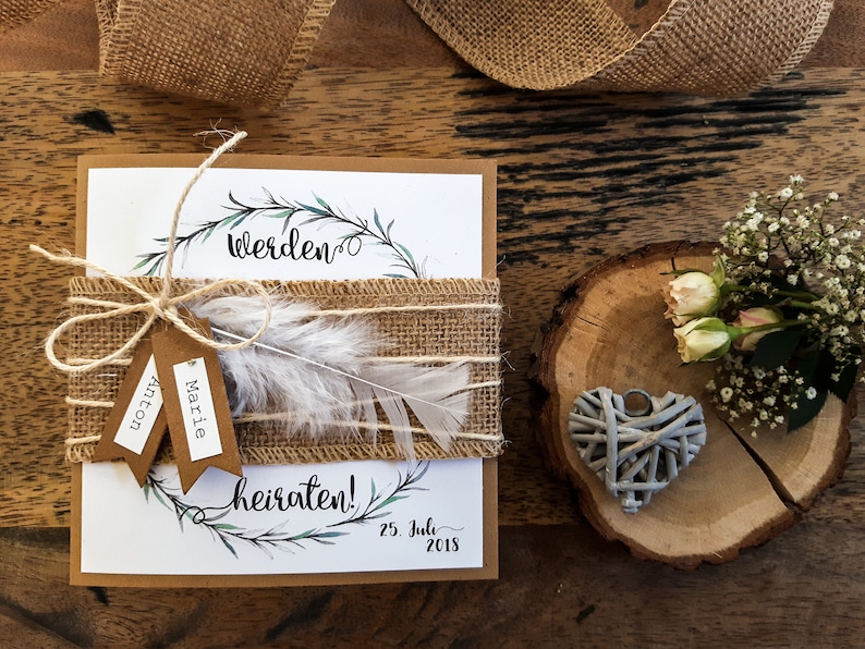 K&ouml;nnte beinhalten: Eine rustikale Hochzeitseinladung mit braunem Papierhintergrund und Juteschnur. Die Einladung zeigt einen Kranz aus gr&uuml;nen Bl&auml;ttern und den Text "Werden" und "heiraten!" in schwarzer Kalligraphie. Das Datum "25. Juli 2018" ist ebenfalls enthalten.