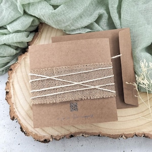 May include: A brown card with a burlap ribbon tied around it. The card has a QR code and the text "Mit Liebe f&uuml;r die Happiness". The card is sitting on a wooden slice.