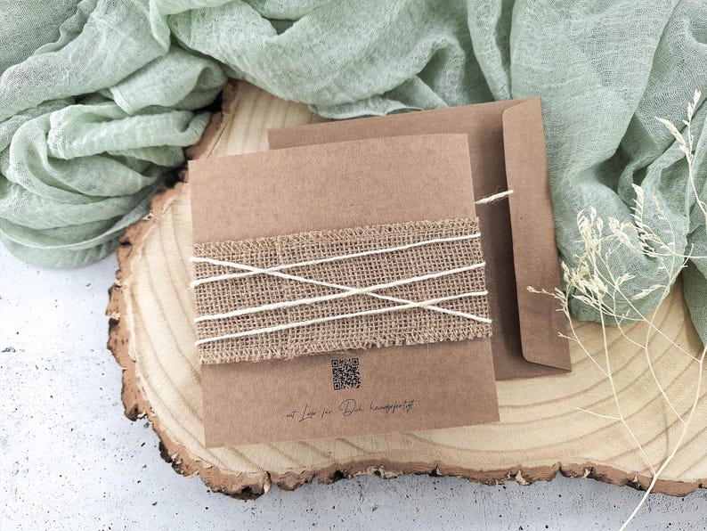 May include: A brown card with a burlap ribbon tied around it. The card has a QR code and the text "Mit Liebe f&uuml;r die Happiness". The card is sitting on a wooden slice.