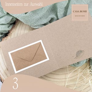 May include: A brown card with a white border around a smaller brown envelope. The card has the text "CASA ROMI" and "ROMANTIC MINDS" printed on it. The card is on a wooden surface with a green fabric in the background.