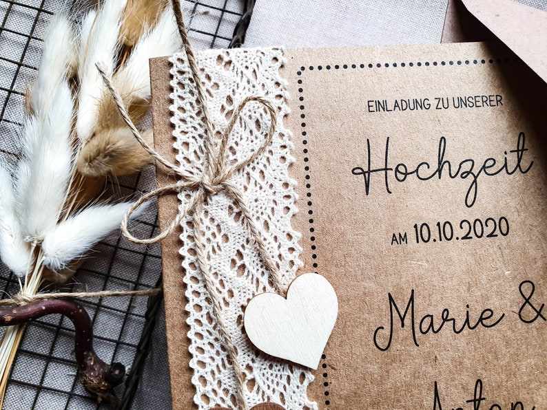 May include: A rustic brown wedding invitation with a lace trim and twine bow. The invitation reads "Einladung zu unserer Hochzeit am 10.10.2020 Marie & Anton".