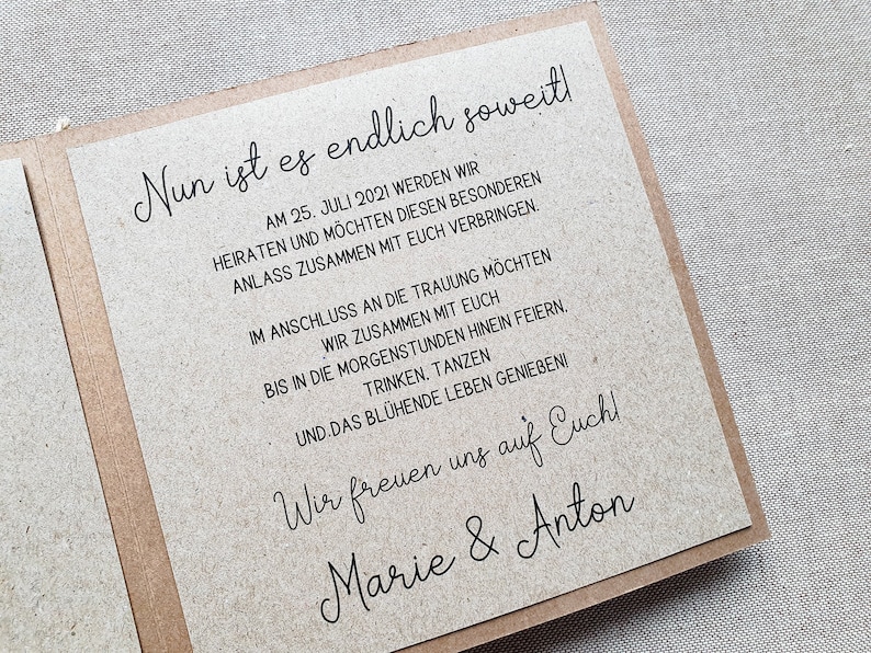 May include: A rustic brown card with black text announcing a wedding. The text reads "Nun ist es endlich soweit!" followed by the date "AM 25. JULI 2021" and details about the wedding celebration. The card is signed "Marie & Anton".