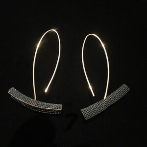 May include: A pair of black and silver earrings with a geometric design. The earrings are made of a thin wire with a small, curved, black piece at the bottom.