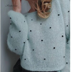 May include: A light blue knitted jumper with black beads throughout the fabric. The jumper has a loose fit and long sleeves.